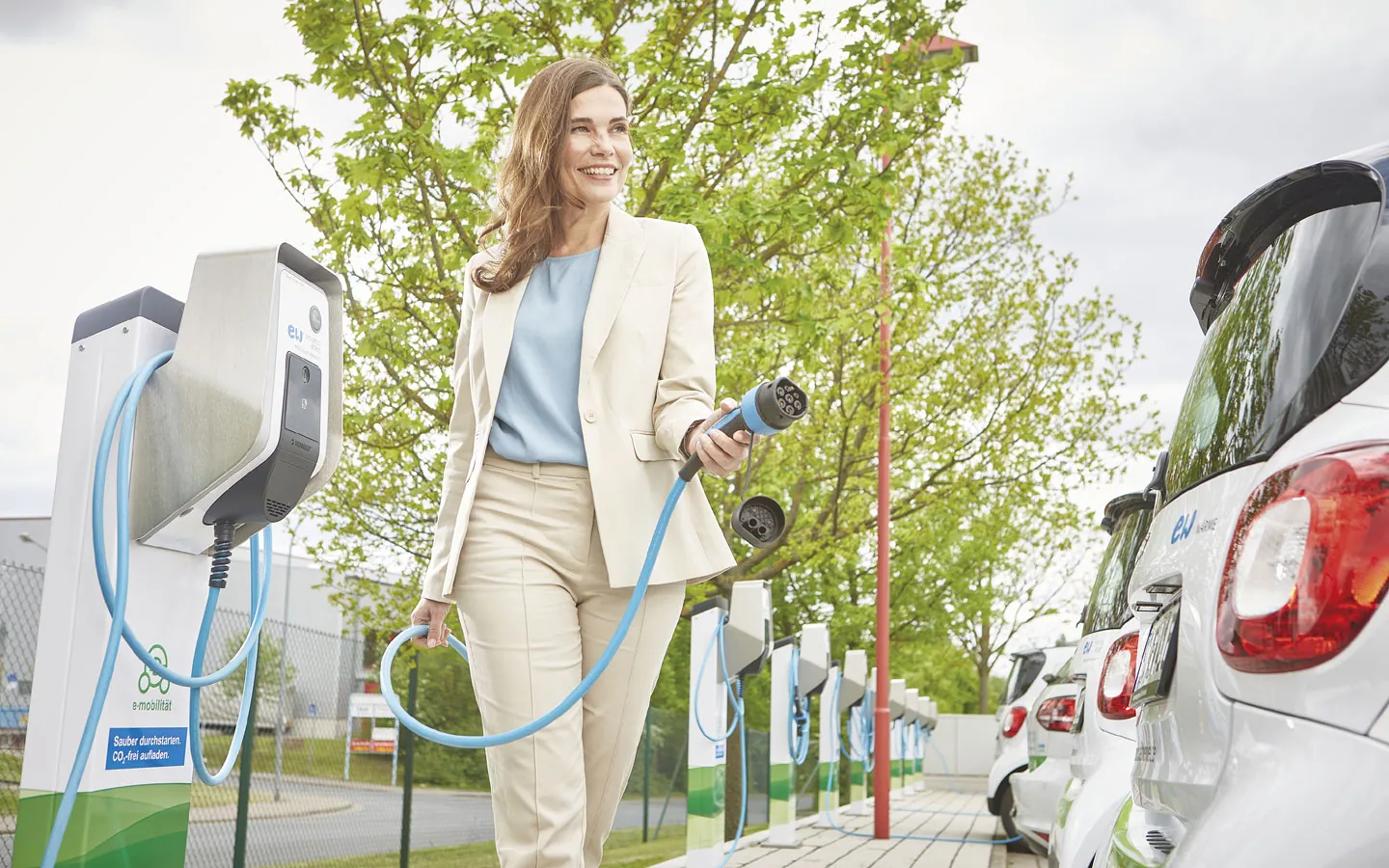 E-Mobilität - Kundin vor Ladestation mit Stecker in der Hand · Elektro Dörr